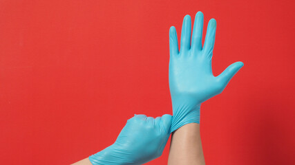 Hand is pulling blue latex gloves or surgical gloves on red background.