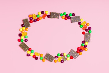Frame of pieces of chocolate, jelly bears and round candies on a pink background. sweets concept for kids. border, top view, copy space.
