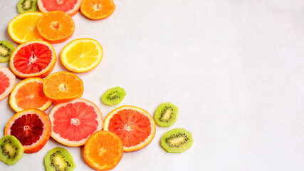 Close-up of sliced red orange, tangerines, green kiwi and grapefruit on a light gray background. Side space for lettering and design.