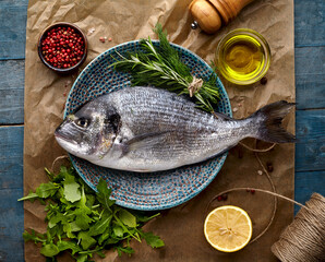 Dorado fish on the wooden  background with olive oil, lemon, arugula  and spices. Top view.