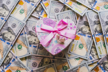 Obraz na płótnie Canvas Pink dotted gift box lies near hundred dollar bills on a background. Birthday, charity.