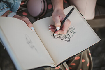 Sketchbook with a drawing of a house close-up. Girl draws with her left hand. - obrazy, fototapety, plakaty