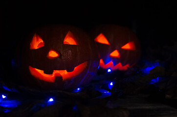 Two glowing pumpkins in the dark in the smoke in the forest close-up. One pumpkin peeks out from behind another. Beautiful background for Halloween.