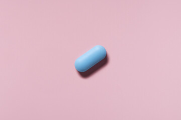 medicine, healthcare and pharmacy concept - blue pill or capsule lies on pink background top view copy space