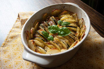 Hearty potato gratin bacon and zucchini,freshly served from the oven on a wooden table.Casserole food,vessel.