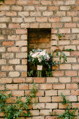 Fototapeta na wymiar bridal bouquet of pink and white peonies, roses, branches of eucalyptus tree, veronica, matthiola and white ribbons in a niche of a brick wall