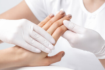 Human hands in protective gloves holding female fingers with beige polish on nails in beauty salon