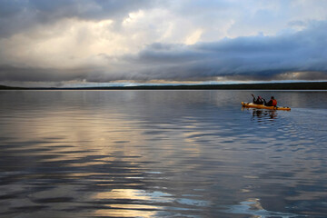 Two tourists on kayak floating on White Sea while dramatic sunset. Republic of Karelia, Russia.