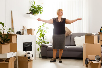 Happy excited mature retired middle aged woman standing in modern living room interior alone with...