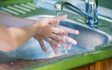 Little child washing hands with clean running water in the park. Coronavirus prevention hand hygiene. Concept hygiene, clean and health care. Flowing water from tap. Outdoor. Natural green background