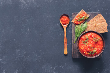 Balkan sauce ajvar in a clay bowl on a dark background. Serbian native, traditional food