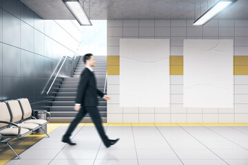Businessman walking in metro station and two blank banners on wall.