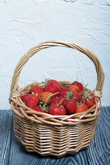 Fototapeta na wymiar Ripe red strawberries in a wicker basket. Against the background of pine boards painted in white and black. Harvest 2020.