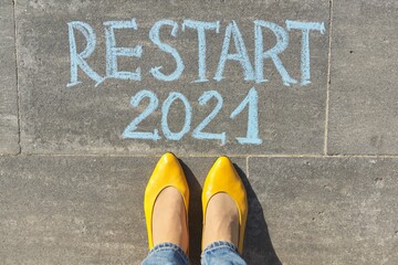 Restart 2021 year concept, top view on woman legs and text written in chalk on gray sidewalk