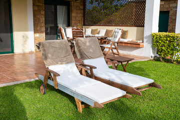 Wooden sunbeds with mattress on a green grass next to the house
