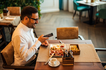 Side view portrait of a smiling elegant man taking picture of his meal on smart phone.