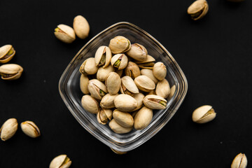 Pistachios in a small plate with scattered nuts of almonds around a plate on a black surface. Pistachio is a healthy vegetarian protein nutritious food. Natural nuts snacks.