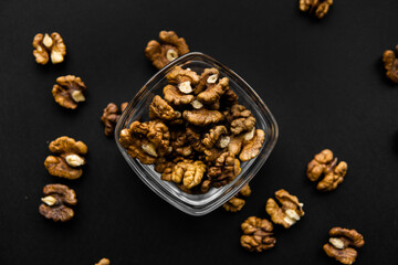 Obraz na płótnie Canvas Walnut in a small plate with scattered shelled nuts which standing on a black surface. Walnuts is a healthy vegetarian protein nutritious food.