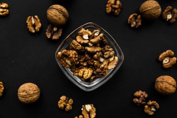 Walnut in a small plate with scattered shelled nuts which standing on a black surface. Walnuts is a healthy vegetarian protein nutritious food.