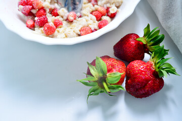 Red juicy strawberries with a plate of porridge on a light table. Healthy breakfast