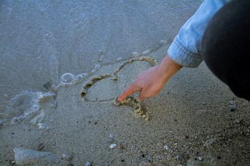 Hand drawing a heart in the sand