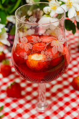 Glass of rose wine with fresh strawberries on  Jasmine flowers, bottle of wine, strawberries, red checkered tablecloth, summer background