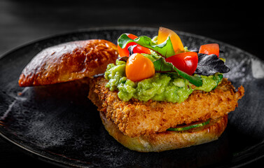 Vegetarian burger with grilled tofu, guacamole sauce and vegetables in plate on black wooden table background