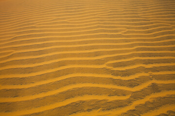 Sand dune in the desert. View on the sandy slope from the top of the sand dune. Sand texture. Sand pattern full frame photography. Sand dune surface in the hot sunny day. Sand ripples close-up. 