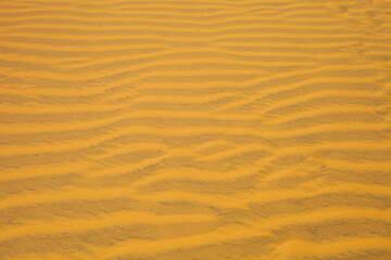 Sand dune in the desert. View on the sandy slope from the top of the sand dune. Sand texture. Sand pattern full frame photography. Sand dune surface in the hot sunny day. Sand ripples close-up. 