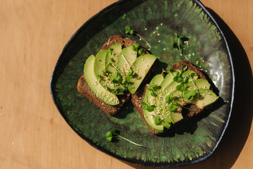 Avocado toast on green plate. Vegetarian food concept. Fresh food at home. Sandwich with avocado and rye bread, sesame seeds and mustard seedings. Top view
