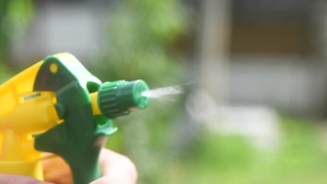 Female hand spray water drops with plastic spray in the garden.