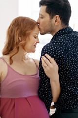 Loving man kissing tenderly his pregnant wife's forehead while holding her hand