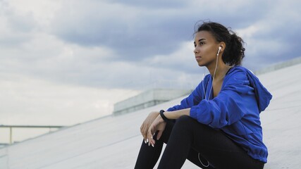 Sporty Afro-american woman in sportswear listening to music and monitoring her progress on a smartwatch