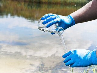 Gloved hand with a flask and a test tube on a background of lake, river, sea.