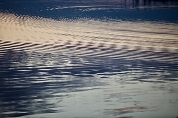 Silver surface of calm water with golden highlights and reflections. Beautiful glowing ripples on water surface close-up. Silver metal surface with abstract pattern close-up. Abstract texture.