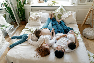 Beautiful pregnant woman lying on the bed with her husband and two awesome kids, boy and girl. Bare...