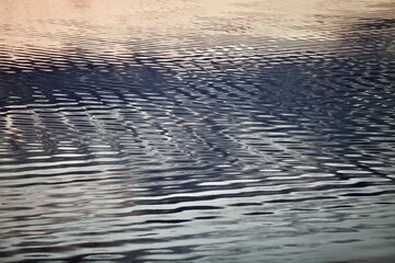 Silver surface of calm water with golden highlights and reflections. Beautiful glowing ripples on water surface close-up. Silver metal surface with abstract pattern close-up. Abstract texture.