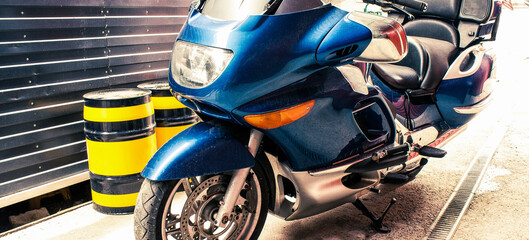 Fototapeta premium Beautiful big blue road bike with large mirrors in a garage with black-yellow oil barrels. Cruise motorbike with comfortable rear seat with wardrobe trunks. Banner for web site
