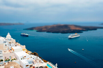 View of Fira Greek town with traditional white houses on Santorini island with cruise ships in sea. Santorini, Greece. Toy camera tilt shift miniature effect