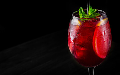 Cold sangria wine in a wine glass with reflection on black background