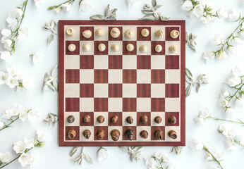 Styled wooden chess game start scene with flowers, flatlay, view from above