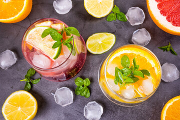 Citrus cold cocktail in transparent glasses on dark background. Around - slices of orange, lemon, grapefruit, ice and mint. Top view, flat lay, minimalism Concept of summer citrus soft drink, cocktail