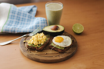 Different cooked egg on avocado sandwich with whole grain bread on wooden board. Smoothie with spinach