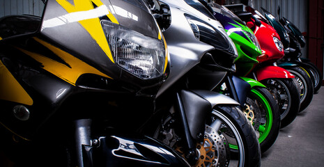 Naklejka premium Colored sports, road beautiful bikes in a motor show, close up. Many motorcycles parked in a store. Sale of used cruise motorbikes in the cabin. Showroom equipment in the garage. Banner for web site