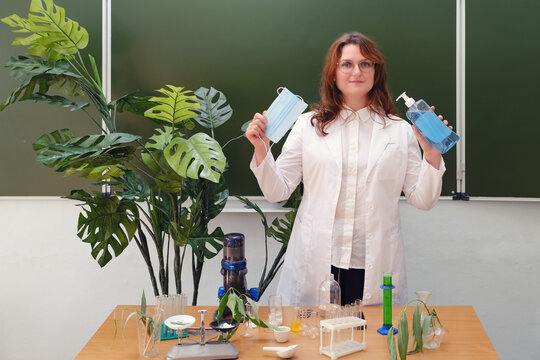The teacher holds a medical mask and sanitizer in the biology class. The ecologist shows correct safety practices when working under quarantine conditions due to coronavirus, copy space.