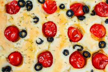 Focaccia with black olives, cherry tomatoes, rosemary and olive oil on a rustic wooden table. 