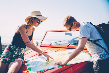 Romantic couple in love reading map on cabriolet checking route for road trip on vacations, woman...