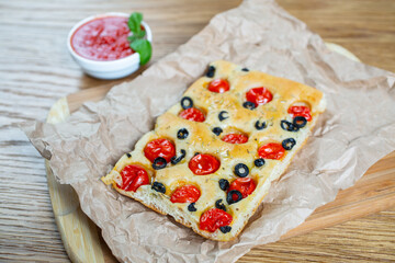 Focaccia with black olives, cherry tomatoes, rosemary and olive oil on a rustic wooden table. 