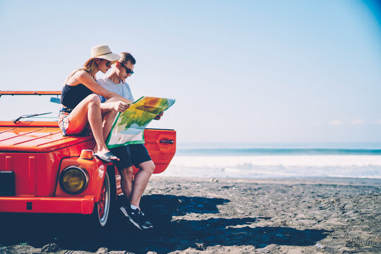 Couple in love searching route for roadtrip spending summer vacation together renting vintage cabriolet,male and female hipsters traveling by automobile on tropical island talking about sightseeing