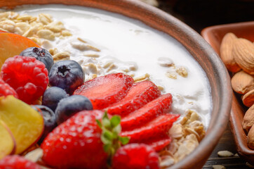 Fruit healthy muesli with peaches strawberry almonds and blackberry in clay dish with yogurt on wooden kitchen table